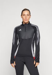 Zwarte sportjack met grijze accenten, halve rits en hoge kraag. Heeft verticale strepen op de mouwen en een aansluitend ontwerp.
