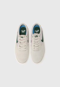 Tenisi Nike SB din suede gri deschis cu swoosh verde închis. Caracteristici: șireturi rotunde, guler căptușit și o limbă albastră cu logo.