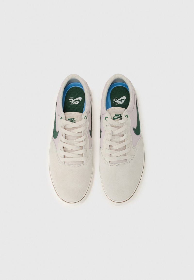 Sneakers Nike SB w jasnoszarej zamszowej cholewce z ciemnozielonym logo Swoosh. Posiada okrągłe sznurowadła, wyściółkę wokół kostki oraz niebieski język z logo.