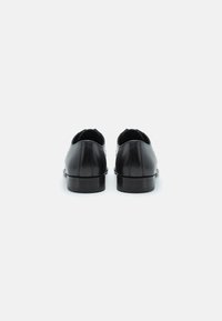 Zapatos de cuero negro con una textura suave, puntera redondeada y tacones bajos. Presentan costuras sutiles a lo largo de las uniones.