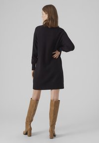 Abito maglione nero a maniche lunghe, con orlo a coste e spacchi laterali, abbinato a stivali in pelle tan al ginocchio con tacco a blocco.