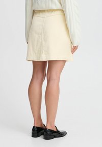 Jupe en velours côtelé crème avec une taille élastique, présentant une coupe droite et une finition à l'ourlet. Assortie à des chaussures noires à petits talons.