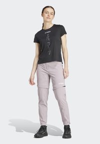 Black short-sleeve t-shirt with reflective logo; light pink zippered pants; black footwear; casual athletic style.