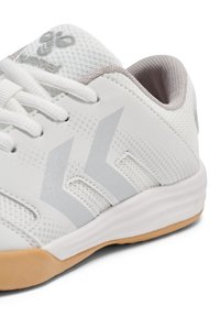 Hvid atletiksko med øvre mesh, grå accenter, afrundet tå og gummisål. Har tre diagonale striber og et minimalistisk design.