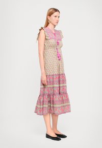 Maxikjole med volangerm, grønn bunn, rosa blomster mønster, utsvingt hem og dekorative dusk; parret med svarte flate sko.