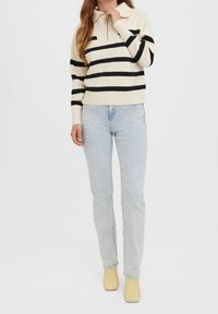 Kremowy sweter dzianinowy z czarnymi poziomymi paskami, z zapięciem na zamek, połączony z jasnoniebieskimi dżinsami i żółtymi klapkami. Prosty i nowoczesny design.