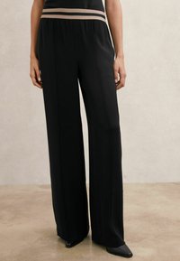 Mustad laiapõhjalised püksid, millel on sile tekstuur, kõrge elastne vöökoht kontrastse beeži triibuga ning kohandatud lõige.