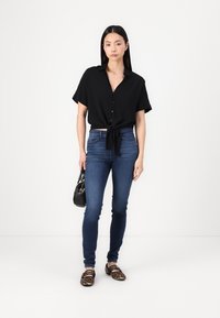 Black short-sleeve button-up shirt tied at the waist, paired with dark blue skinny jeans and animal print flats. Accessories include a small black handbag.