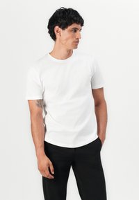 T-shirt en coton blanc à manches courtes, col rond, texture lisse et coupe décontractée, associé à un pantalon noir.