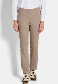 Beige slim-fit broek met een gladde textuur, voorzien van een platte tailleband en subtiele stikdetails, gecombineerd met lichtgekleurde sportschoenen.