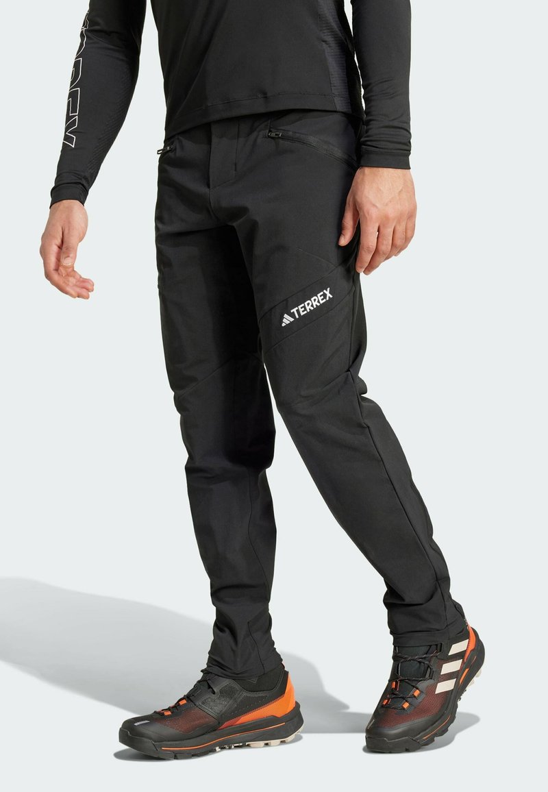 Zwarte buitenbroeken met een slank ontwerp, ritszakken en een gestructureerde afwerking, gecombineerd met multikleurige sportschoenen.