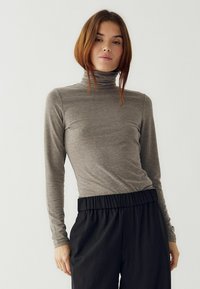 Pelēks garām piedurknēm, augsta apkakle, izgatavots no mīksta materiāla, ar pieguļošu dizainu. Kombinēts ar melnām, elastīgas jostas biksēm kontrastā.