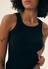 Black ribbed tank top with a round neckline and fitted design, showcasing textured fabric and racerback style.
