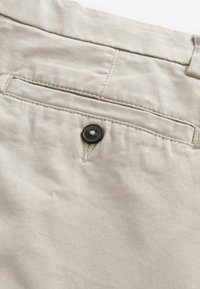 Pantalones de algodón beige con un bolsillo trasero con un botón negro y un detalle de costura neat. Textura suave y diseño de pierna recta.