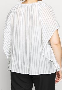 Top de rayas blancas y grises con un corte holgado, escote redondo y mangas anchas y vaporosas. La tela parece ligera y con textura.