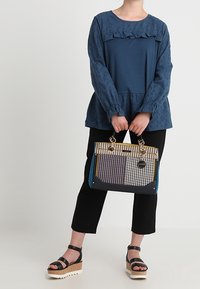Blusa blu navy con scollatura arricciata e motivo texture, pantaloni neri, sandali con zeppa e borsa a tracolla con motivo multicolore.