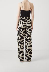 Zwarte kanten top en brede broek met een contrasterend gedurfde zwart-witte abstracte print. Elastische tailleband, lichte stof.