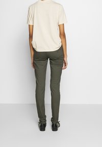 Camiseta de manga corta beige, corte relajado; pantalones ajustados verde oliva; zapatos negros con cordones; diseño sencillo, sin patrones ni herrajes visibles.