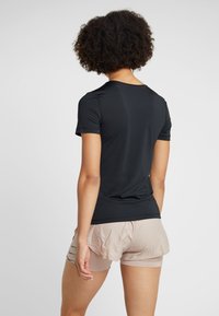 Camiseta atlética negra de manga corta. Textura suave, diseño ajustado. Combinada con pantalones cortos beiges claros que presentan un patrón texturizado.