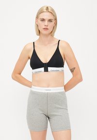 Čierna podprsenka s nastaviteľnými ramienkami a predným zapínaním; šedé boxerky z bavlneného zloženia s bielym pásom s logom Calvin Klein.