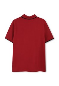 Polo rouge à manches courtes, en tissu texturé, avec un col noir, et un ourlet droit. Étiquette visible en bas à gauche.