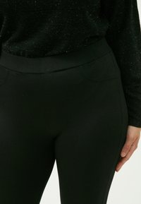 Zwarte stretchy leggings met een soepele textuur, hoge tailleband en twee subtiele voorkeurs. Ideaal voor comfort en casual draag.