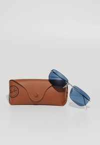 Sončna očala Ray-Ban z modrimi lečami, kovinskim okvirjem in rjavim teksturiranim usnjenim etuijem z gumbom za zapiranje in logotipom blagovne znamke.