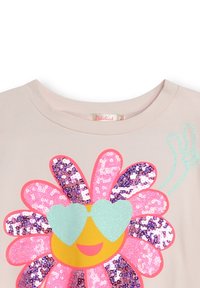 Camiseta rosa claro con un gran diseño de flor de lentejuelas coloridas, gafas de sol brillantes azules y un acento de signo de paz en turquesa.