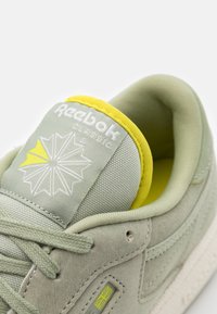 Ljusgrön mockaskor med en texturerad yta, gula accenter, vadderad krage och en vit logotyp på tungan. Har platta snören.