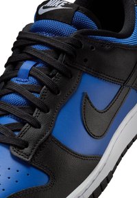 Le scarpe Nike nere e blu sono realizzate in materiali in pelle e mesh, presentano una superficie liscia, una forma arrotondata, lacci neri e una suola in gomma bianca con un dettaglio del logo.