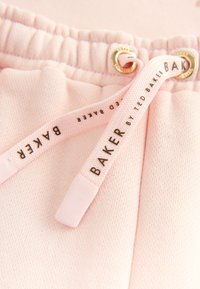 Gros plan sur une ceinture élastique rose pâle avec des cordons assortis imprimés avec "BAKER by Ted Baker" en texte noir.