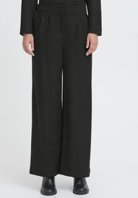 Pantaloni neri a gamba larga realizzati con tessuto strutturato, caratterizzati da pieghe frontali e tasche laterali, abbinati a stivali neri alla caviglia.