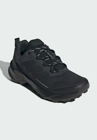 Scarpa da trekking nera con tomaia in mesh e materiale sintetico, superfici testurizzate, lacci riflettenti e suola robusta per una migliore trazione.