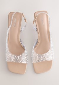Paire de sandales slingback beige à bout ouvert avec des brides transparentes ornées de petites perles blanches et argentées, talons carrés plats, taille 40.