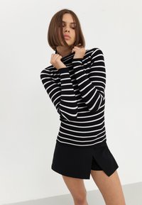 Črno-bela prugaasta rebrasta turtleneck pulover z dolgimi rokavi, v kombinaciji s črnimi kratkimi hlačami s stranskim razporkom. Enostaven, oprijet dizajn.