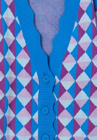 Cardigan blu con bordi scallop e bottoni sopra un motivo geometrico a rombi argyl di blu, lavanda e diamanti di lilla chiaro.