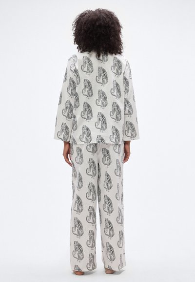 Λευκή πιτζάμα με μαύρο τύπωμα τίγρης, με μακριά μανίκια και άνετο παντελόνι, κατασκευασμένη από ελαφρύ ύφασμα.