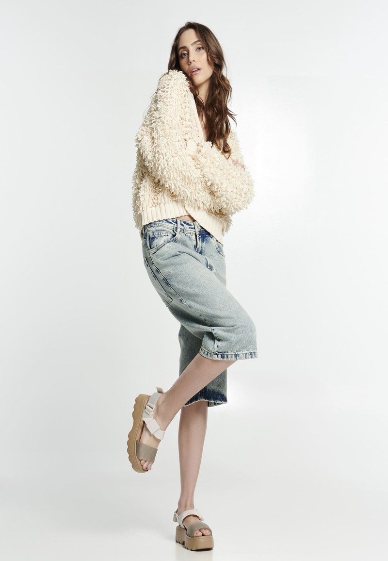 Maglione in crema a texture, culotte in denim blu chiaro e sandali beige con platform e cinturini. Stile semplice, vestibilità rilassata e casual.