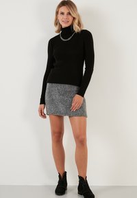 Maglione a collo alto a coste nere abbinato a una mini gonna in maglia grigia. Stilizzato con stivaletti neri alla caviglia con dettagli a borchie. Collana in argento.