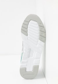 Semelle d'une chaussure de sport blanche et grise avec motifs de la semelle et logo New Balance visible en bas.