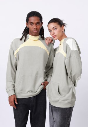 Light gray hoodies with contrasting yellow and white accents, features a front pocket, and relaxed fit. Worn by two models.