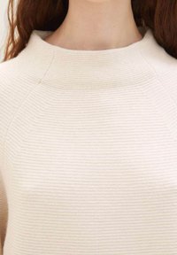 Pull couleur crème avec une texture côtelée, encolure bateau et détails subtils de coutures aux épaules.