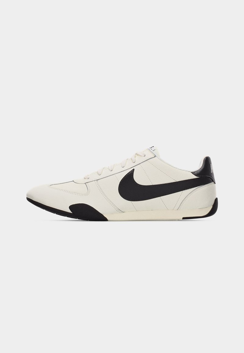 Weißer Sneaker mit niedrigem Schaft, schwarzem Nike-Swoosh, schwarzer Ferse und Akzenten an der Außensohle, seitlich auf einem einfarbigen Hintergrund gesehen.