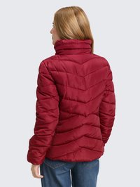 Rote wattierte Jacke mit Chevron-Steppung, hohem Kragen, glatter Textur und Seitentaschen, kombiniert mit blauer Jeans, Ansicht von hinten.