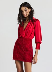 Abito rosso con un top in satin dal profondo scollo a V e maniche a sbuffo, che si trasforma in un tessuto floreale testurizzato nella gonna.