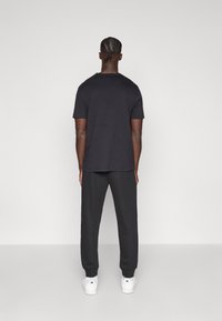 Μαύρο κοντομάνικο μπλουζάκι και σκούρο παντελόνι φόρμας, κατασκευασμένα από απαλό ύφασμα, με ριμπ μανσέτες. Λευκά αθλητικά παπούτσια ολοκληρώνουν το σύνολο.