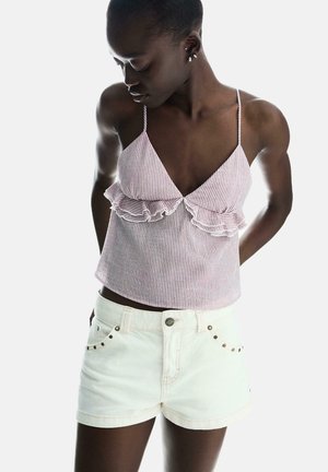 Top court rayé rouge et blanc avec des volants, bretelles fines. Assorti à un short en denim blanc avec des accents métalliques et une coupe ajustée.