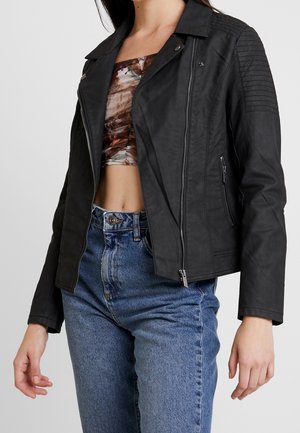 Zwarte neplederen jas met een getailleerd ontwerp, ritsaanpassing aan de voorkant en ribbelaccenten op de schouders. Gecombineerd met hoogstaande blauwe jeans.