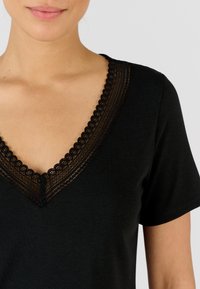 Camiseta negra con un escote en V profundo que presenta un intrincado borde de encaje. Tela suave con mangas cortas y una sutil textura en el escote.