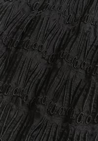 Tissu noir avec des motifs de points en relief, ovales allongés et bouclés formant un motif texturé répétitif.